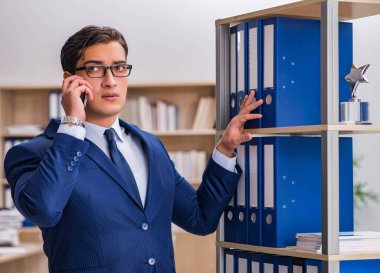 Dosyalarla rafın yanında duran genç adam.