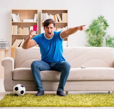 Evdeki kanepede oturup futbol izleyen bir adam.