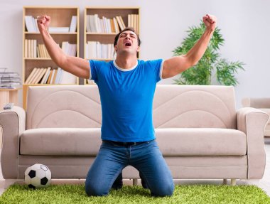 Evdeki kanepede oturup futbol izleyen bir adam.