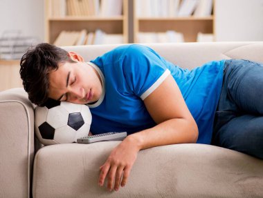 Evdeki kanepede oturup futbol izleyen bir adam.