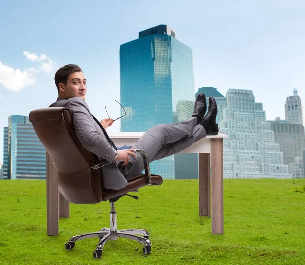 Бизнесмен сидит на траве с видом на город — стоковое фото