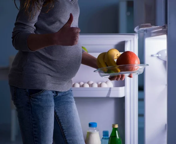 Mujer embarazada cerca de la nevera en busca de comida y aperitivos por la noche —  Fotos de Stock