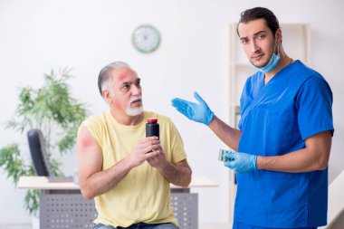 Yaralı yaşlı adam genç erkek doktor travmatoloğu ziyaret ediyor.