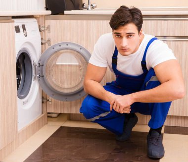 Tamirci mutfakta çamaşır makinesini tamir ediyor.