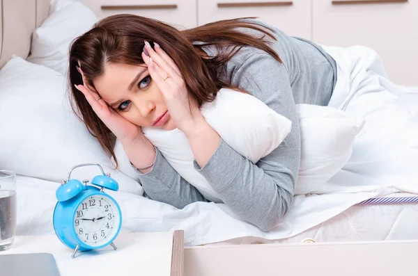 Giovane donna sdraiata sul letto nel concetto di gestione del tempo — Foto Stock