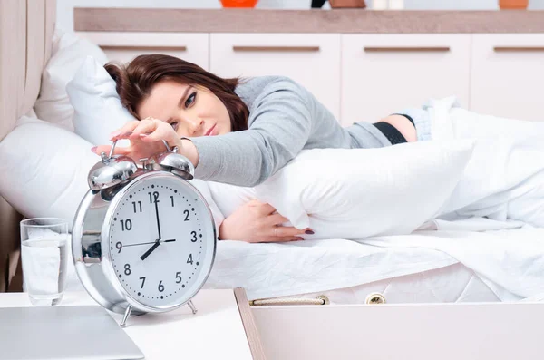 Mujer joven acostada en la cama en concepto de gestión del tiempo —  Fotos de Stock