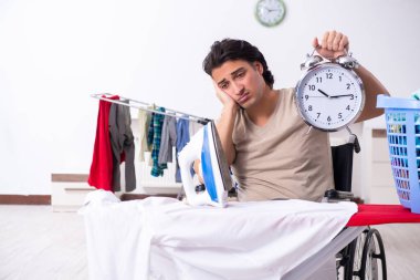 Tekerlekli sandalyedeki genç adam evde ütü yapıyor.