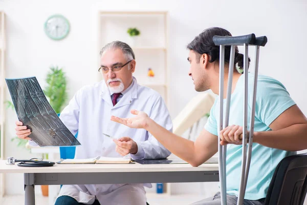 Joven pierna lesionada paciente masculino visitando viejo médico — Foto de Stock