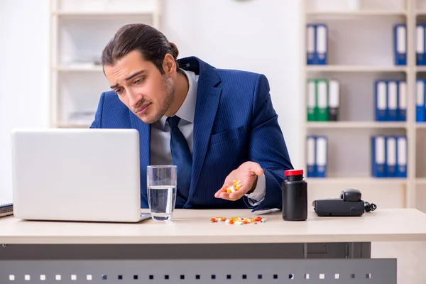 Jonge mannelijke werknemer en veel pillen op het bureau — Stockfoto