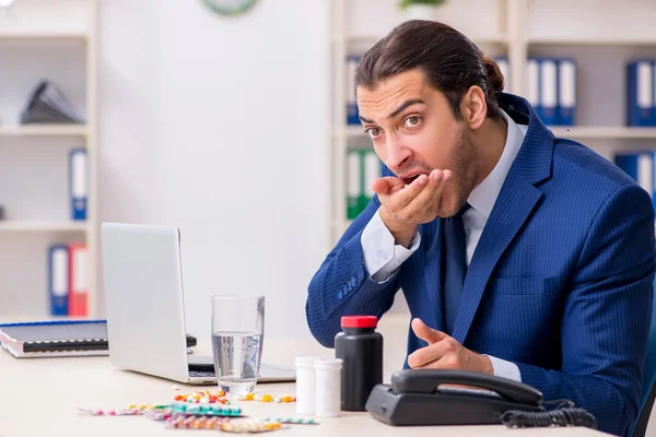 Young male employee and a lot of pills on the desk — Stock Photo, Image