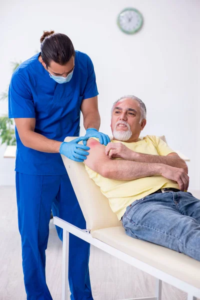 Yaralı yaşlı adam genç erkek doktor travmatoloğu ziyaret ediyor. — Stok fotoğraf