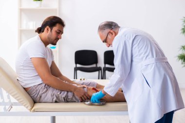 Yaralı adam ilk yardım konseptinde yaşlı doktoru ziyaret ediyor.