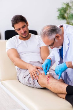 Yaralı adam ilk yardım konseptinde yaşlı doktoru ziyaret ediyor.