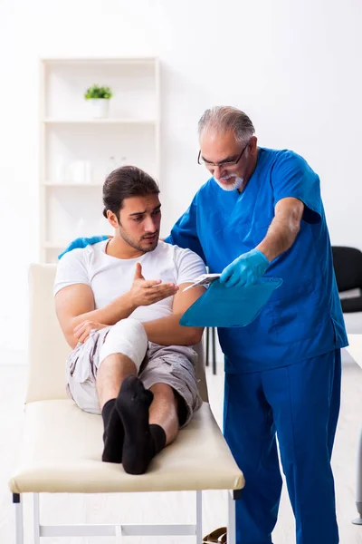 Leg injured man visiting old doctor in first aid concept — Stockfoto