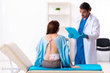 Yaralı genç kadın genç erkek doktoru ziyaret ediyor.