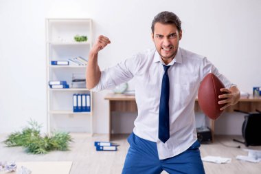 Genç erkek çalışan ofise rugby topu atıyor.
