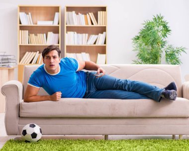 Evdeki kanepede oturup futbol izleyen bir adam.