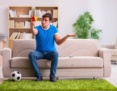 Evdeki kanepede oturup futbol izleyen bir adam.