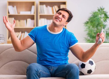 Evdeki kanepede oturup futbol izleyen bir adam.
