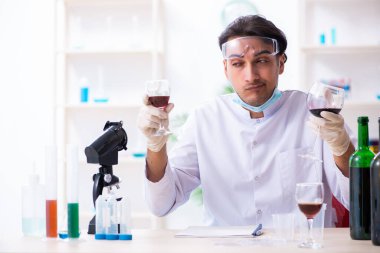Erkek kimyager laboratuvarda şarap örneklerini inceliyor.