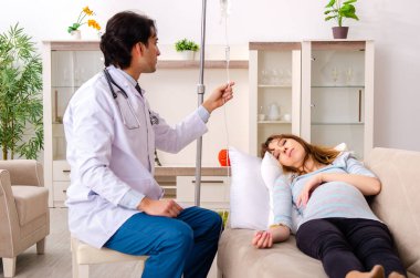 Genç, yakışıklı doktor hamile kadını ziyaret ediyor.