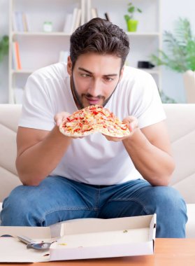 Pizza yiyen adam evde yemek yiyor, dinleniyor.