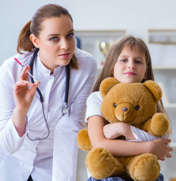 Mujer médico femenino examinando poco linda chica con juguete oso —  Fotos de Stock