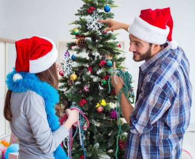 Genç aile Noel ağacını mutlu bir vesileyle süslüyor.