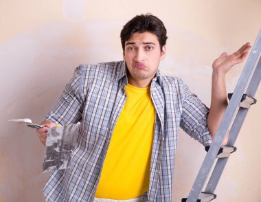 Evdeki duvara alçı yapıştıran genç adam.