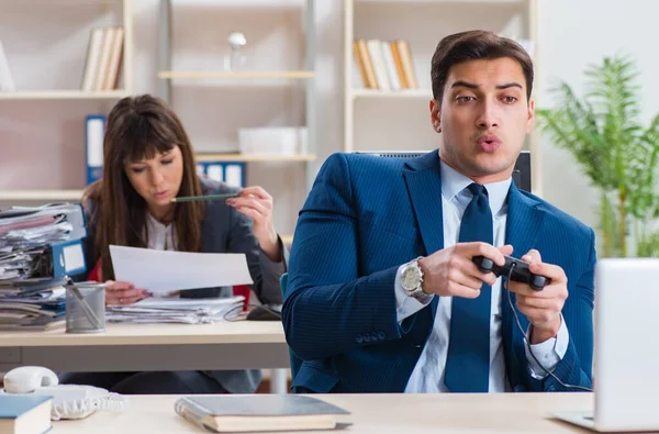 Man playing games in office while colleague is busy