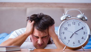 Yataktaki adam alarm yüzünden uykusuzluk çekiyor.