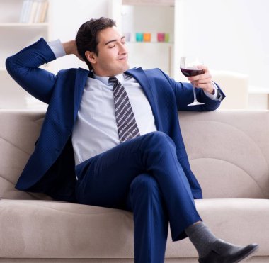 İş adamı evde oturmuş şarap içiyor.