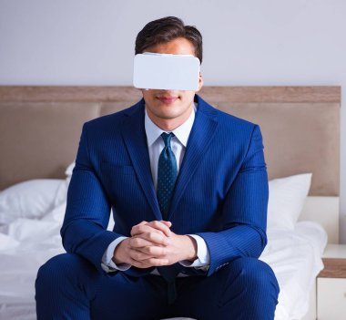 Yatak odasında sanal gerçeklik kulaklığı takan bir iş adamı.