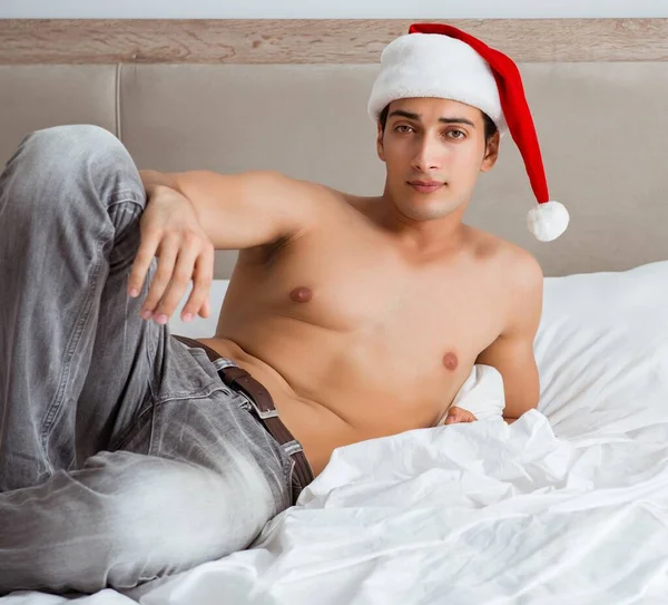 Νεαρός σέξι άντρας που φοράει καπέλο Σάντα στο κρεβάτι — Φωτογραφία Αρχείου