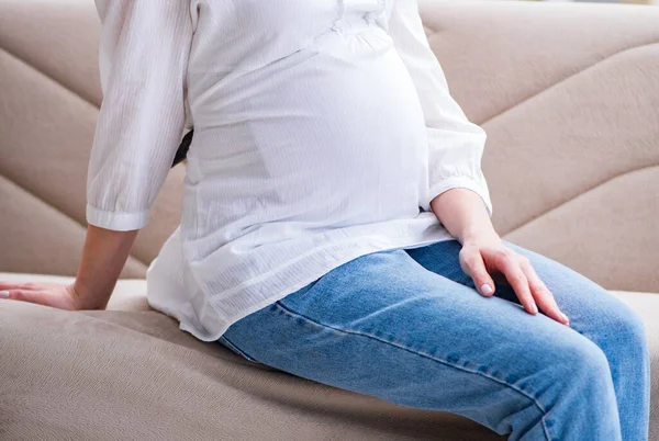Mujer embarazada con barriga sentada en un sofá en casa —  Fotos de Stock