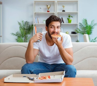 Pizza yiyen adam evde yemek yiyor, dinleniyor.