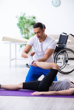 Erkek fizyoterapist yerde yaralı bir kadınla egzersiz yapıyor.