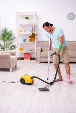 Genç yaralı adam evi temizliyor.