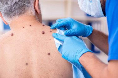 Yaşlı adam genç erkek doktor dermatoloğu ziyaret ediyor.