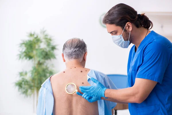 Homem velho visitando jovem médico dermatologista masculino — Fotografia de Stock