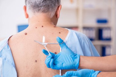 Yaşlı adam genç erkek doktor dermatoloğu ziyaret ediyor.