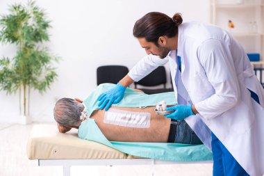 Yaşlı adam genç erkek doktoru ziyaret ediyor.