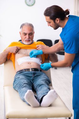 Yaşlı adam genç erkek doktoru ziyaret ediyor.