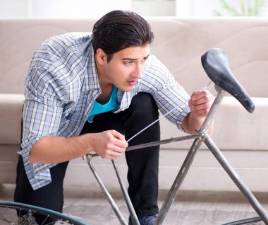 Evde bisiklet tamir eden genç bir adam.