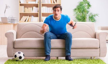 Evdeki kanepede oturup futbol izleyen bir adam.