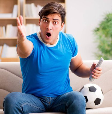 Evdeki kanepede oturup futbol izleyen bir adam.