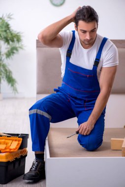 Genç erkek müteahhit eve mobilya kuruyor.