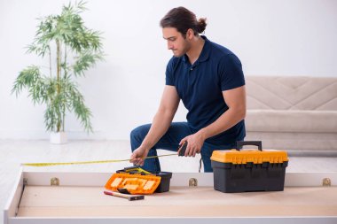 Genç erkek müteahhit eve mobilya kuruyor.