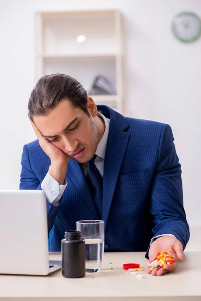 Young male employee and a lot of pills on the desk — Stock Photo, Image