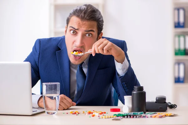 Jovem funcionário do sexo masculino e um monte de comprimidos na mesa — Fotografia de Stock